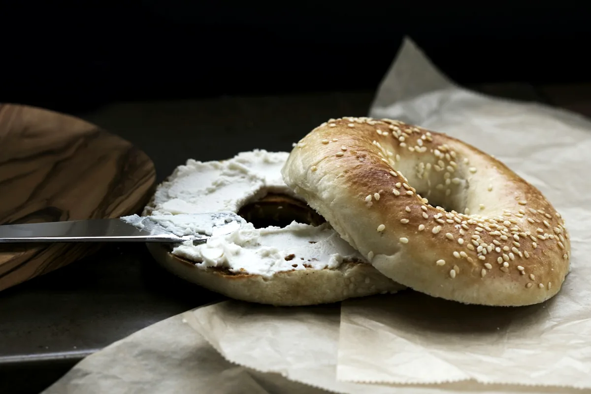 A sesame bagel beside a spread of cream cheese on paper