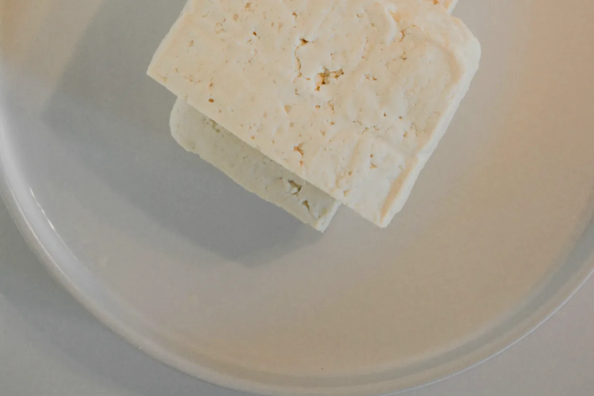 A plain white block of tofu on a white plate