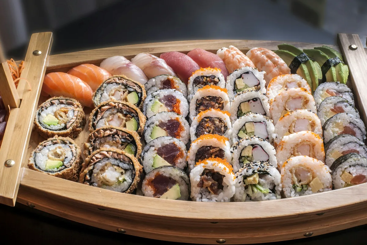 A large wooden boat platter filled with rows of cut sushi pieces