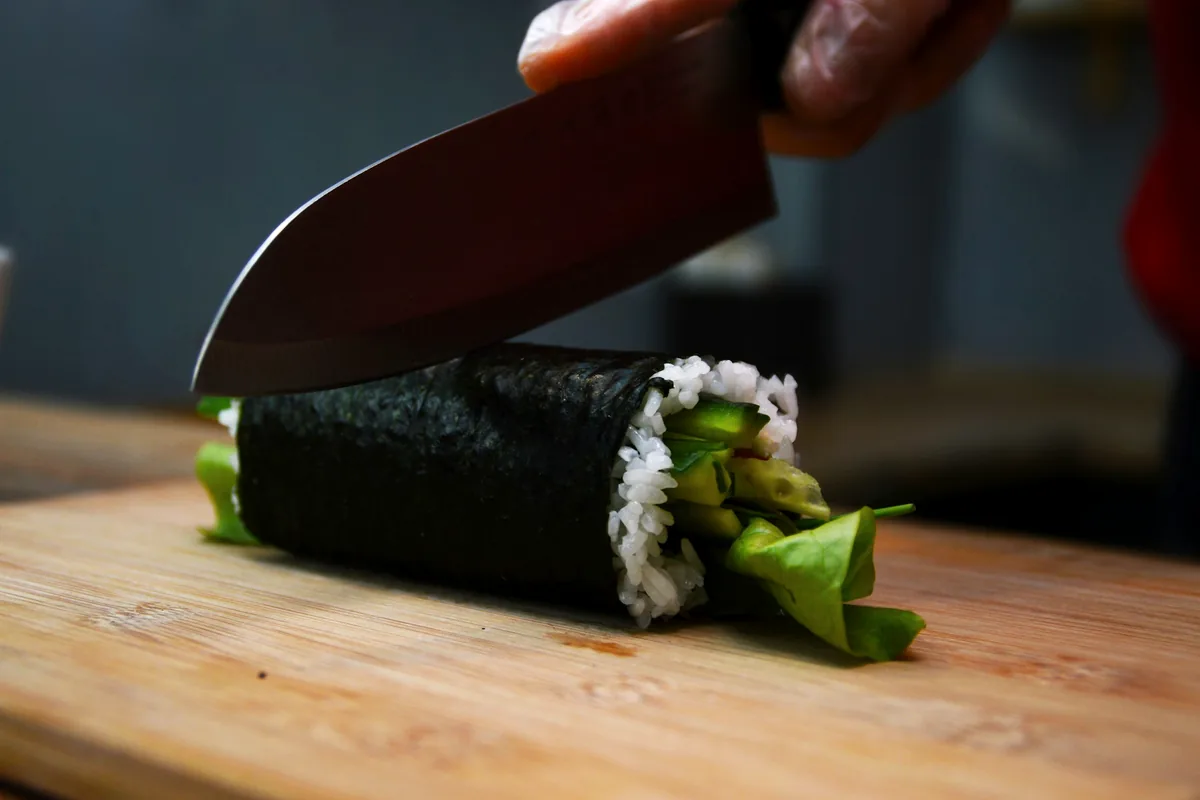 A knife blade cutting down through a rolled sushi cylinder