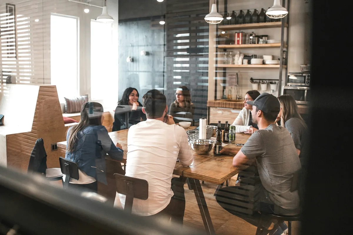 People eating along a long shared table in an open room