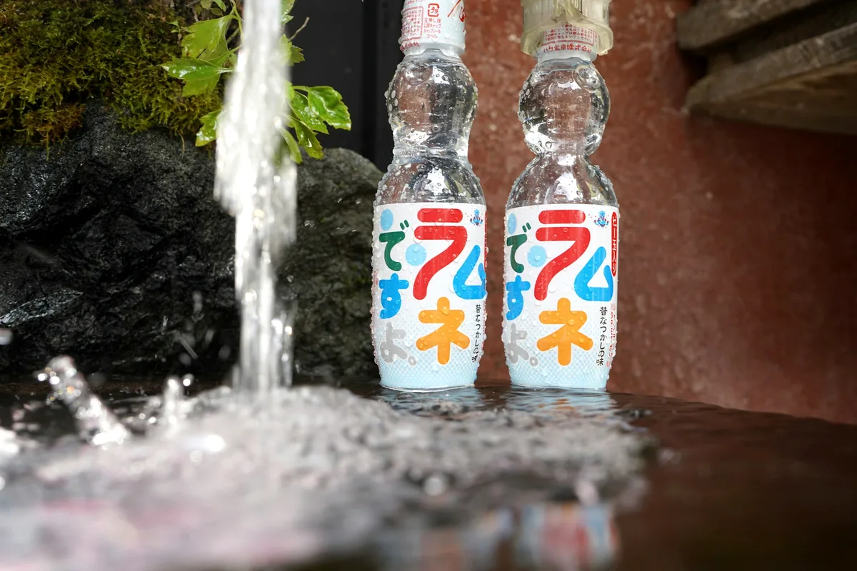 A glass ramune bottle with its marble neck, held up outdoors