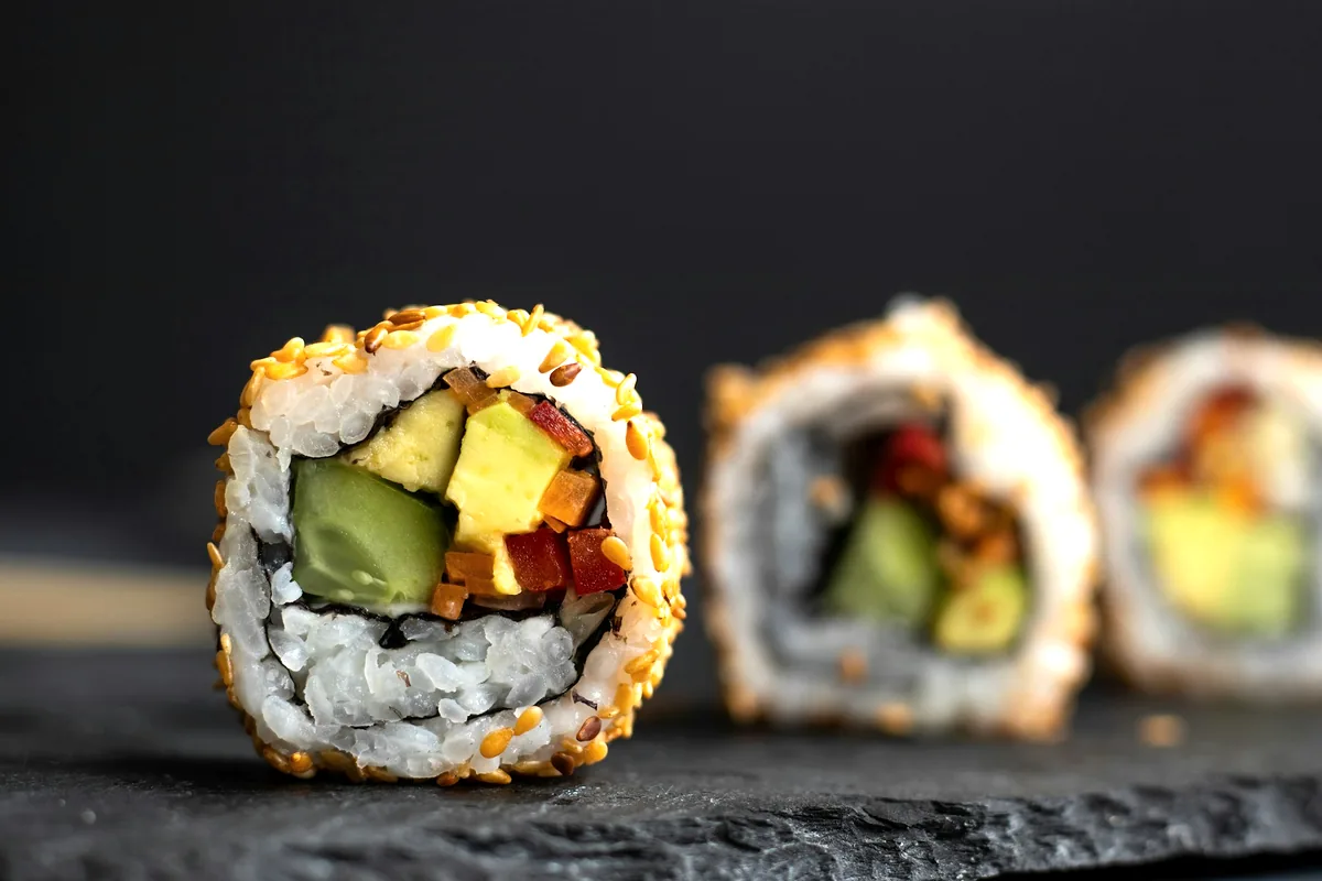 Cut sushi rolls filled with avocado on a dark board