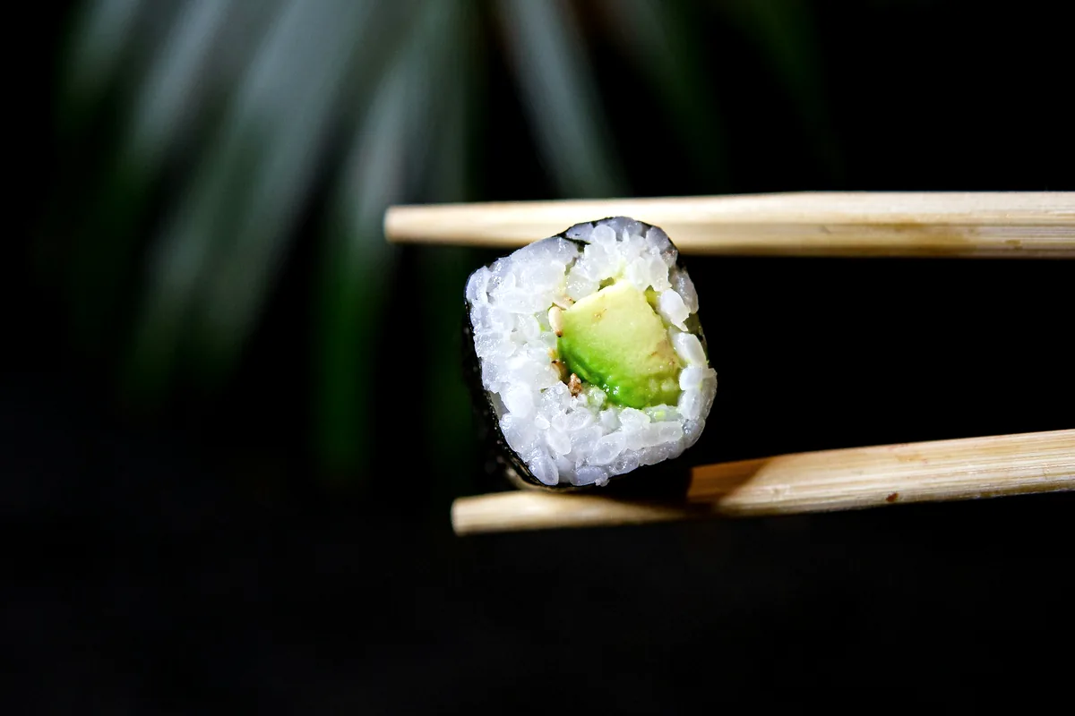 Chopsticks lifting a piece of avocado roll