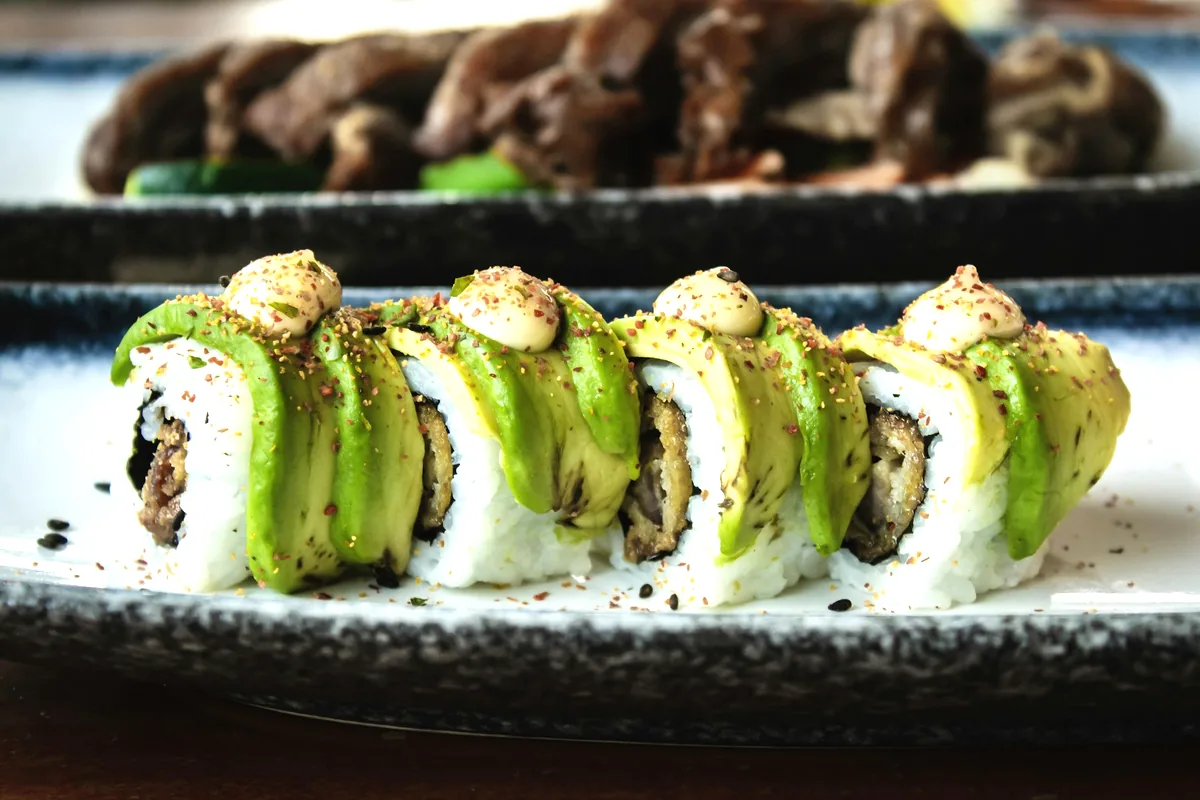 A cut roll covered with overlapping slices of avocado