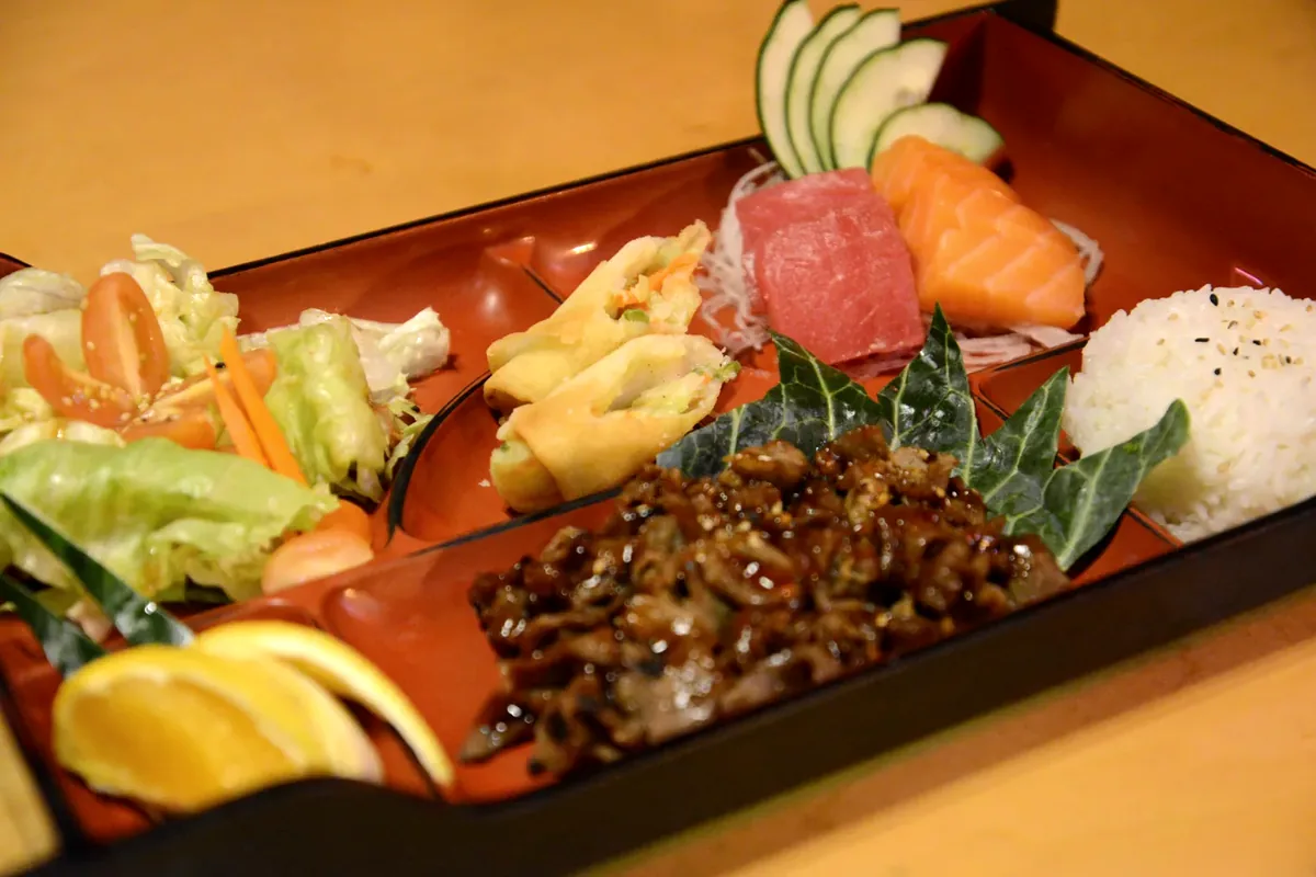 A bento box combination with sashimi, tempura, teriyaki and rice in a divided tray