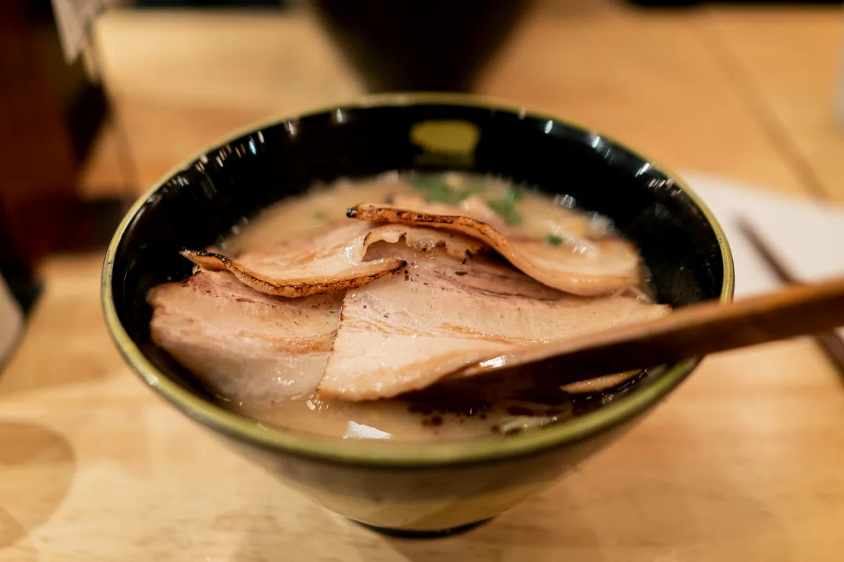 Thin slices of braised pork belly laid across the surface of a bowl of broth