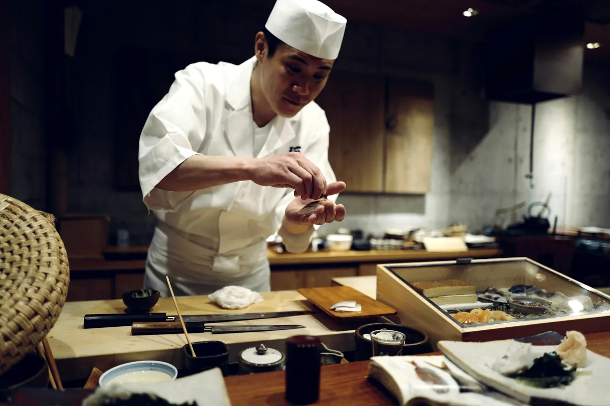 A sushi chef assembling food behind a wooden counter