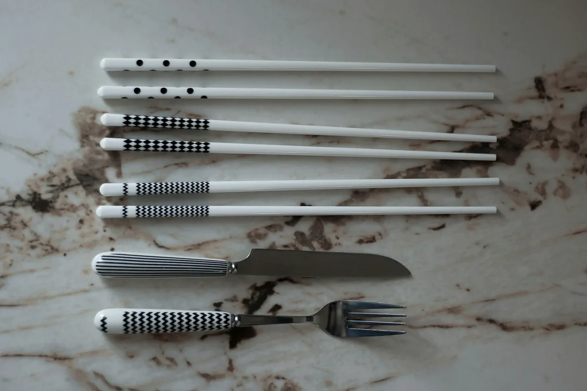 Chopsticks laid alongside a knife and fork on a marble surface