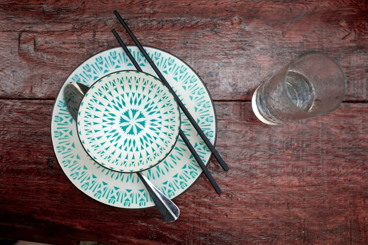 Chopsticks resting beside a patterned plate on a dark table