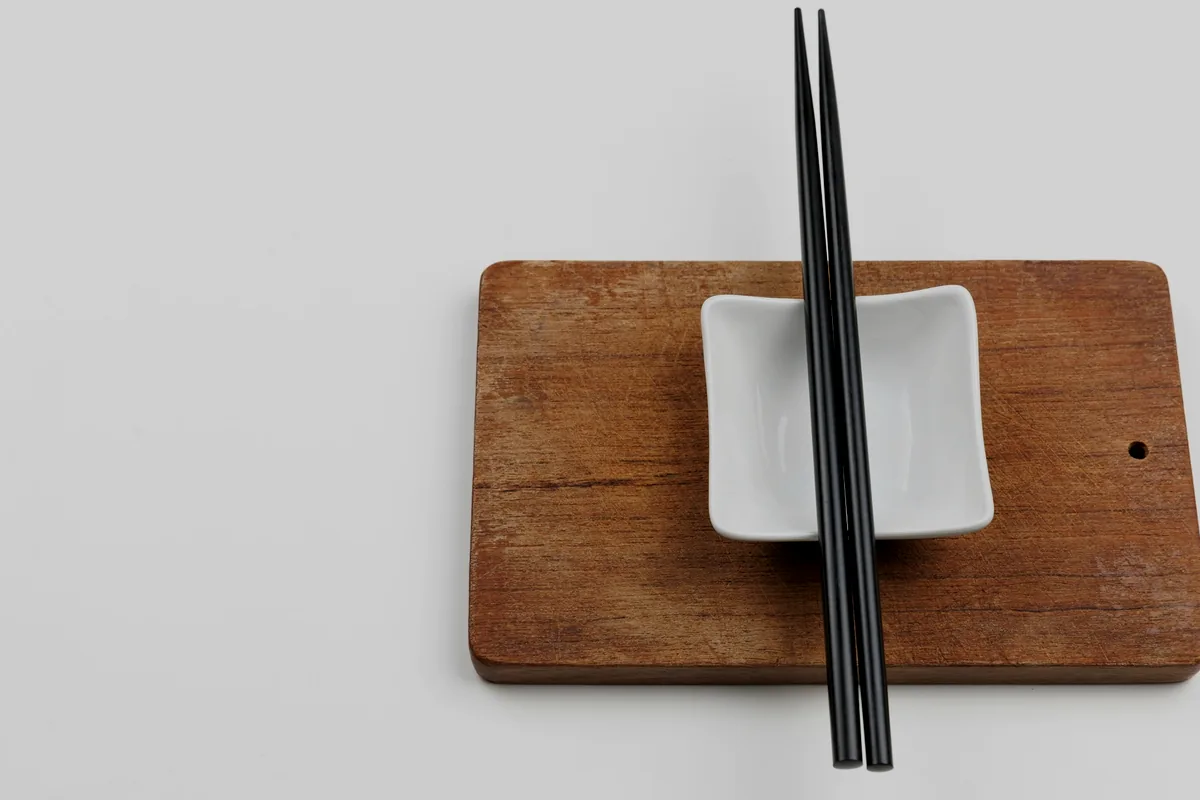 A pair of chopsticks and a small sauce dish on a wooden board