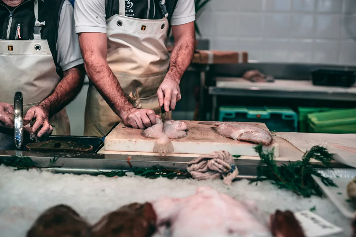 Hands cleaning and trimming fish at a preparation counter