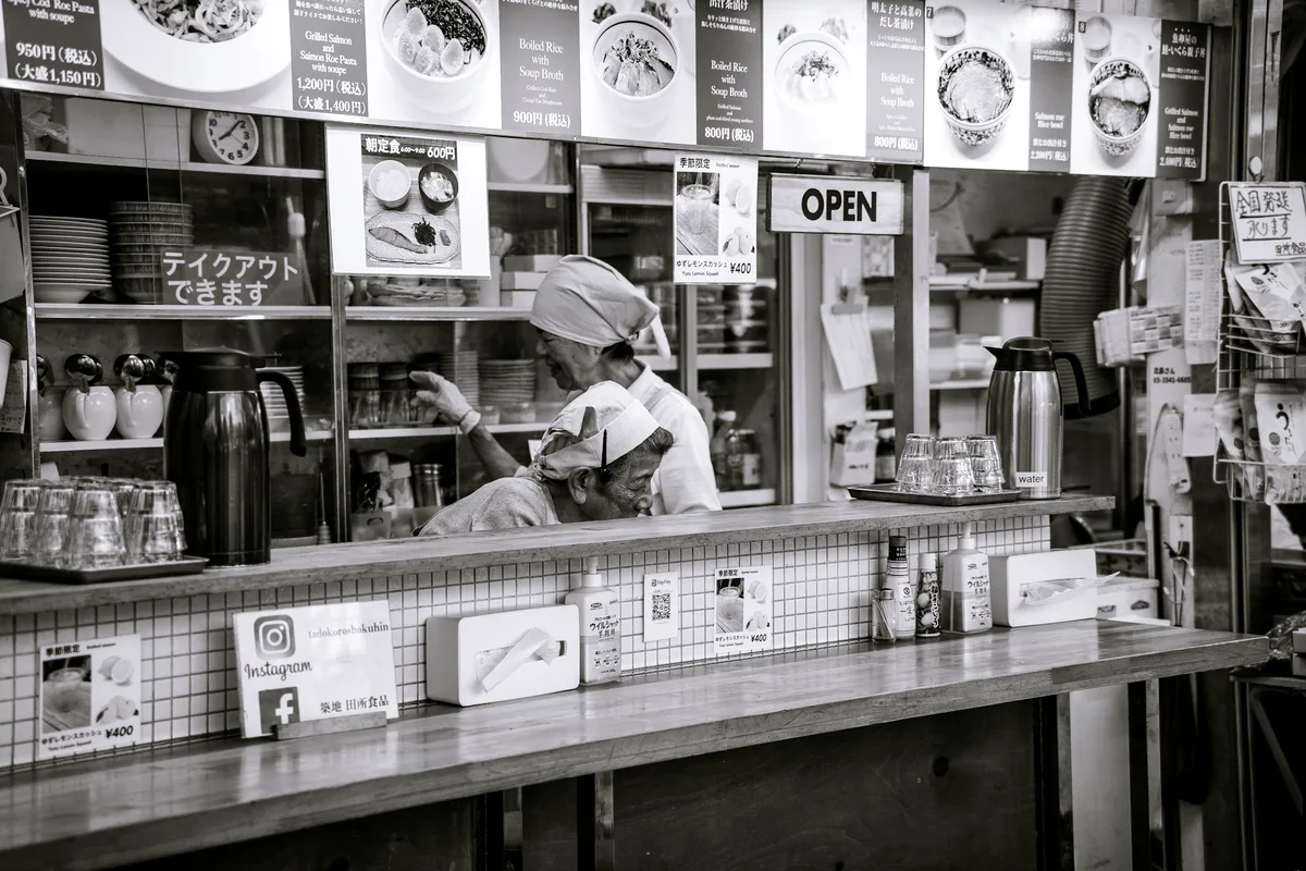 A black and white view of a cook working behind a small counter