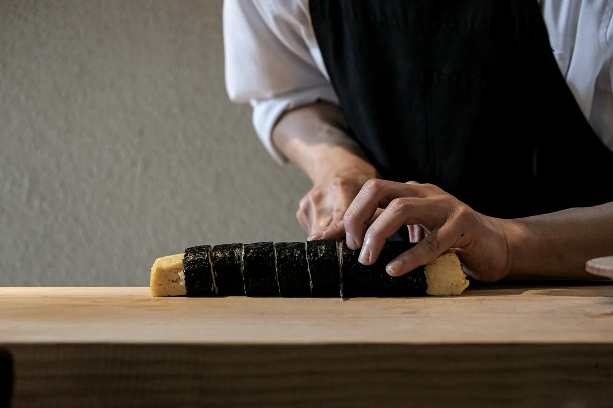 Hands cutting a rolled cylinder into pieces on a board