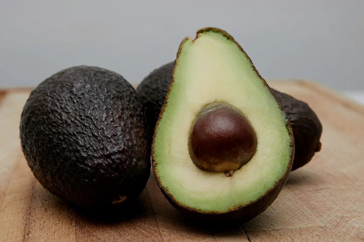 Dark-skinned avocados, one cut open to show the flesh