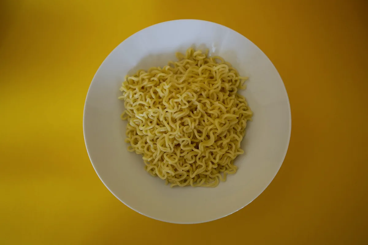 A round block of dried instant noodles on a plate against yellow