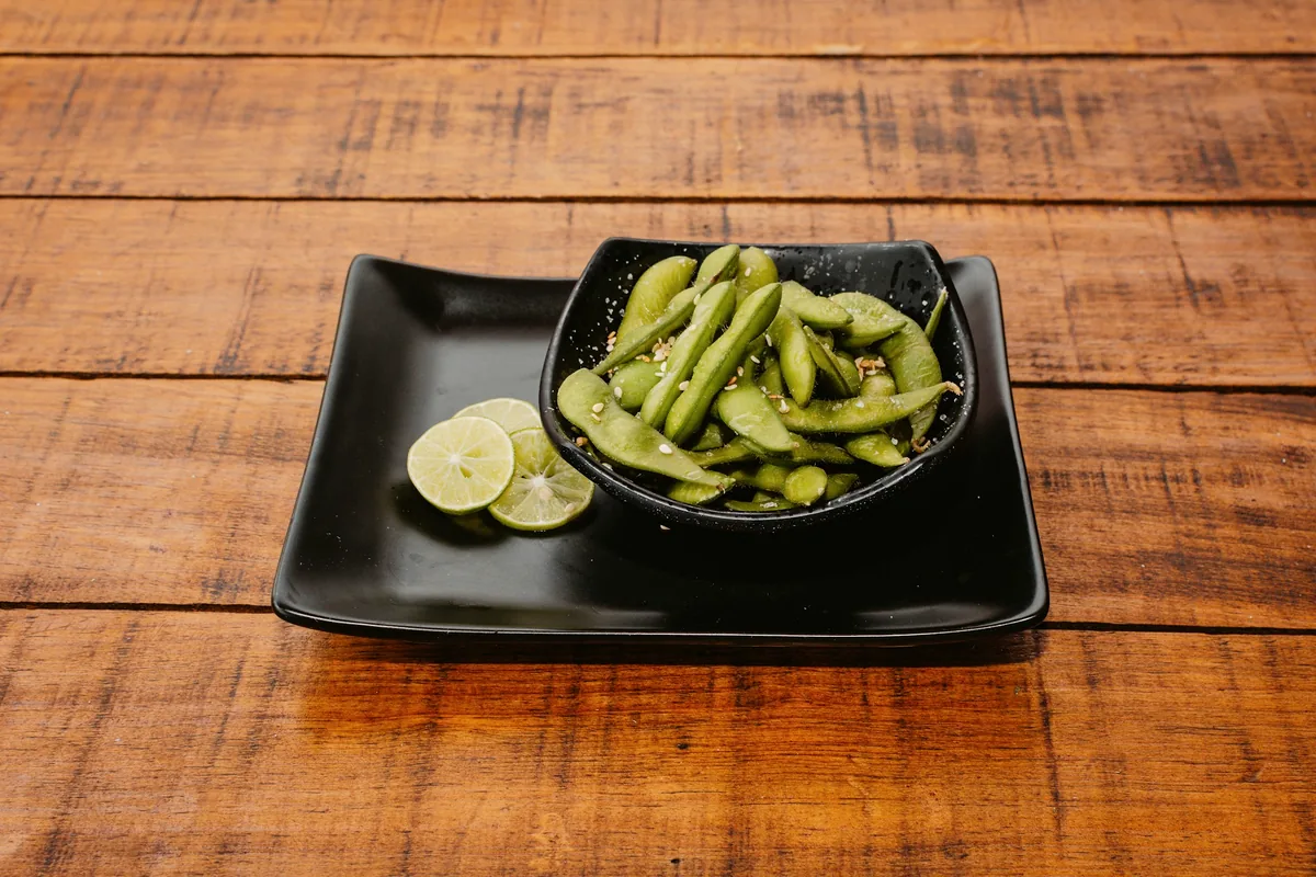 Edamame pods on a black dish with a wedge of lime