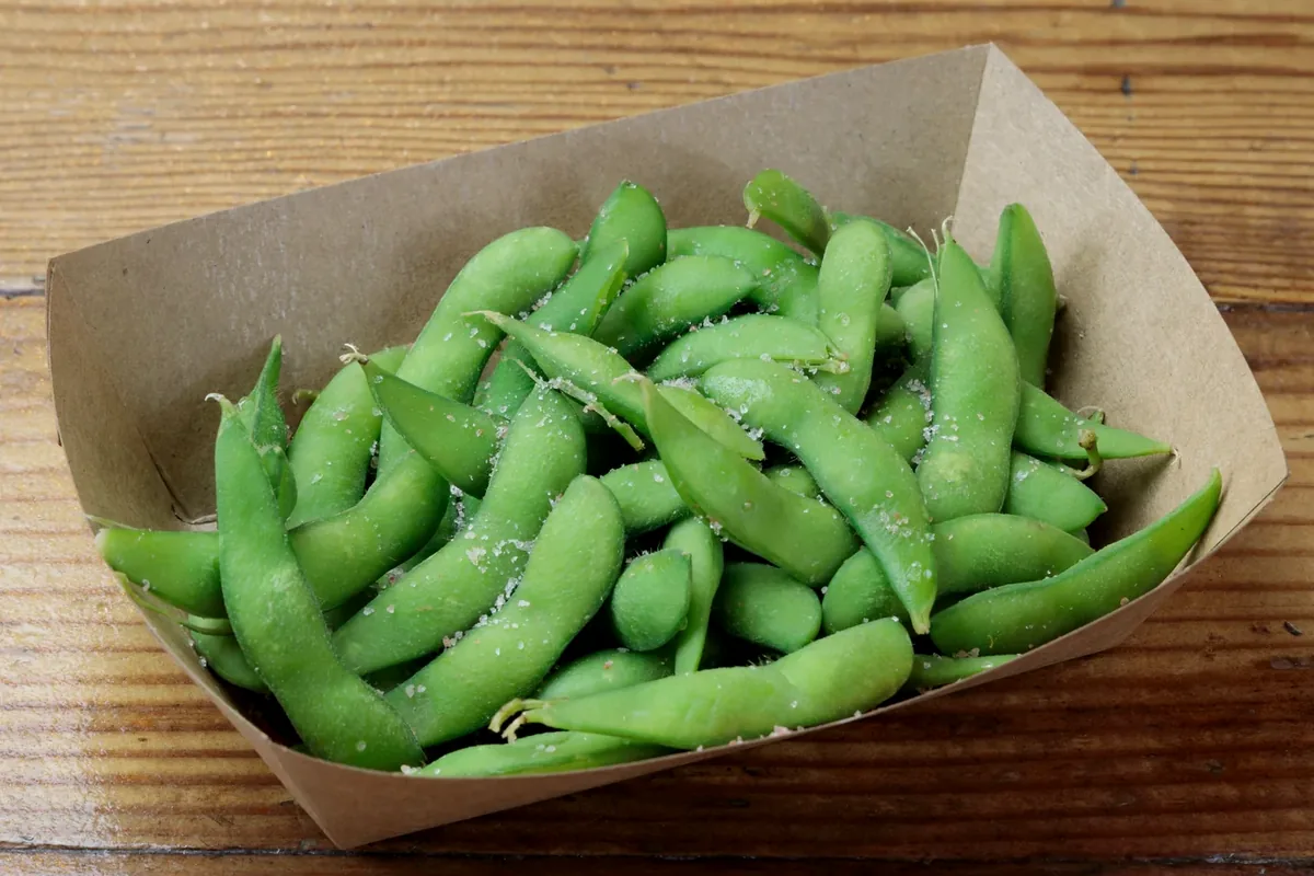A serving of salted edamame pods in a paper-lined basket
