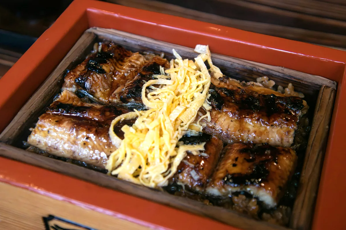 Whole glazed eel fillets arranged in a serving box with shredded egg