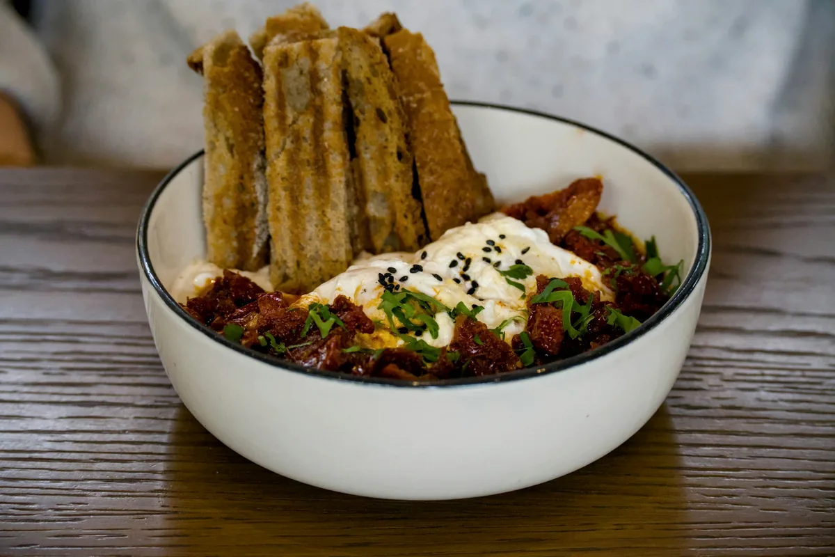 Strips of glazed eel over rice in a white bowl, scattered with sesame