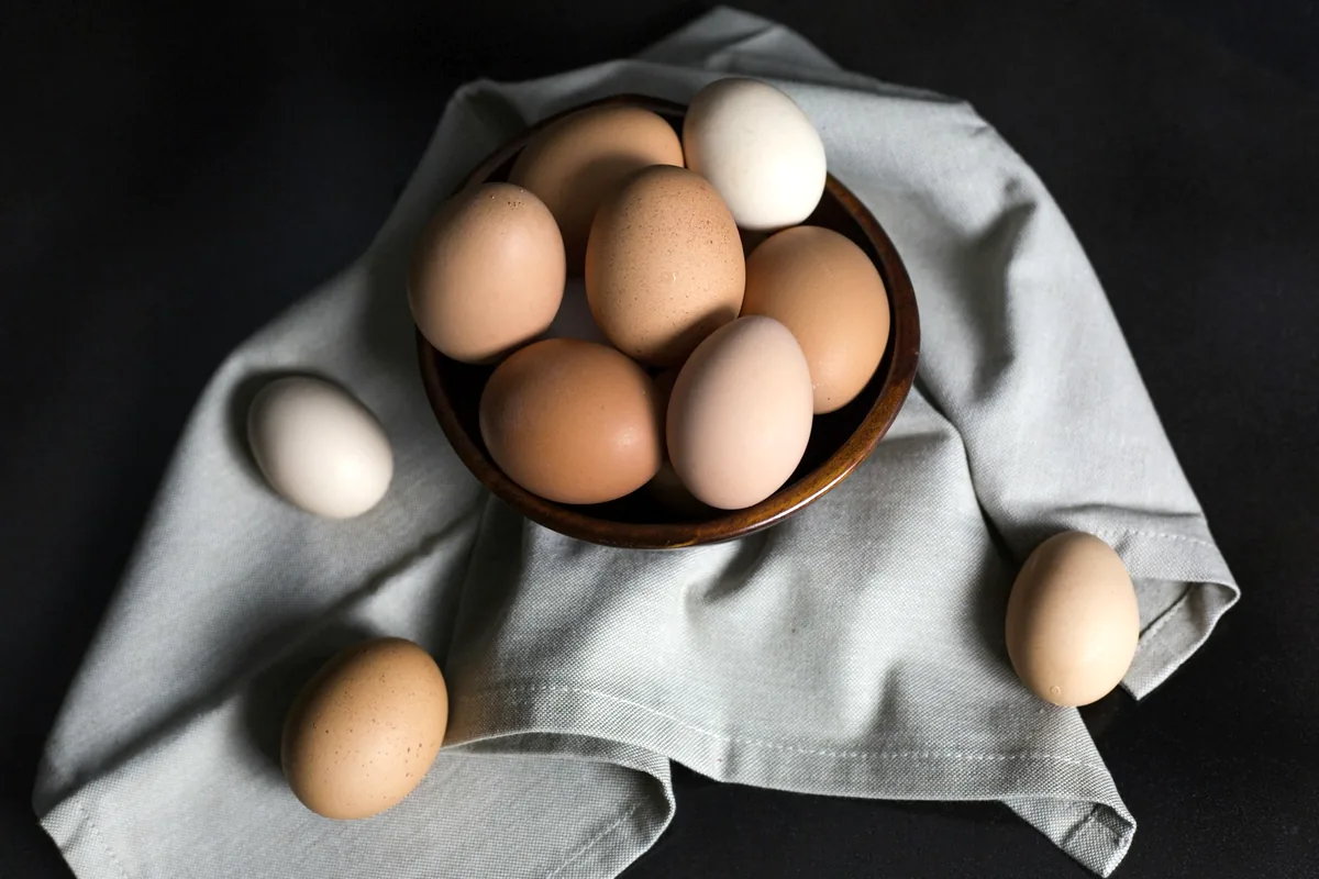 Brown eggs gathered in a bowl on a dark cloth