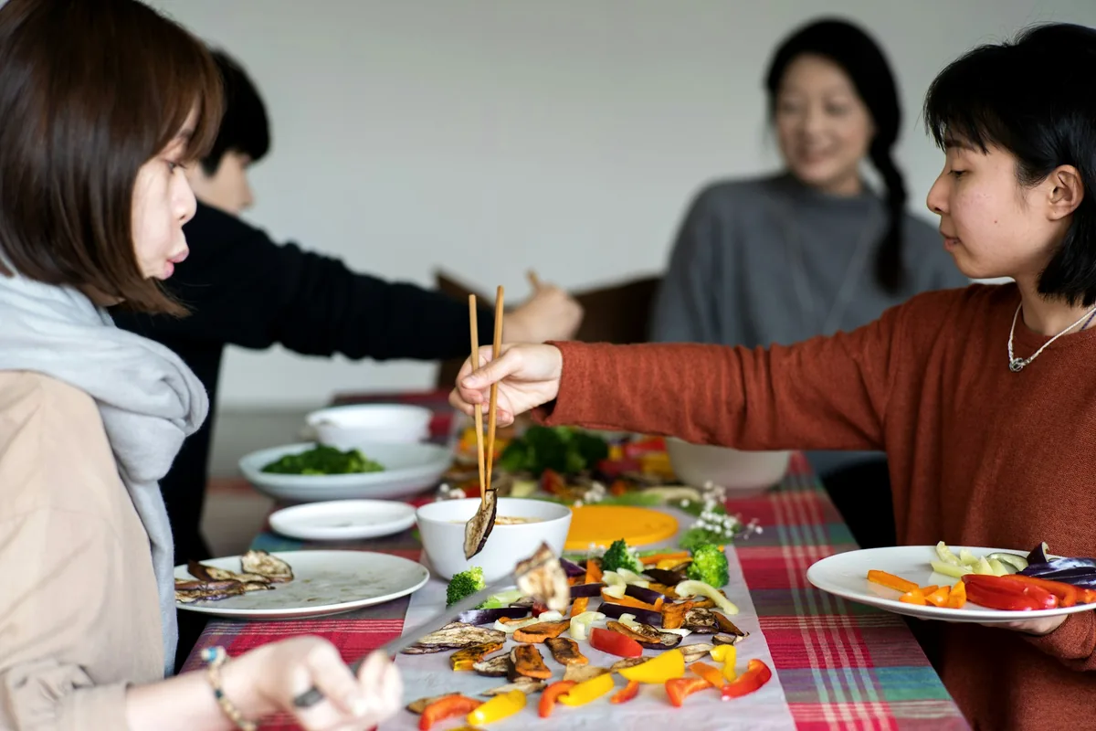 Two people reaching across a shared table of small dishes with chopsticks