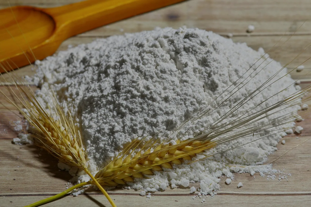 A mound of wheat flour on a board with ears of wheat beside it