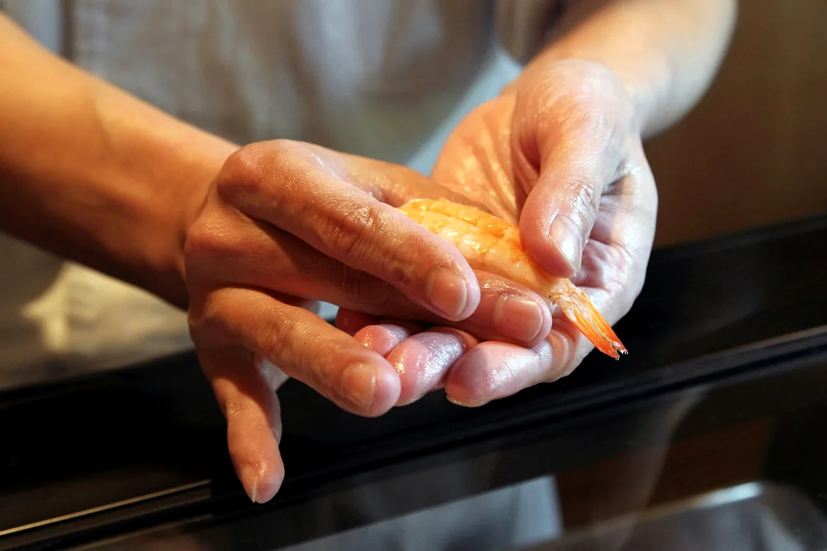 A pair of hands pressing a small block of rice into shape