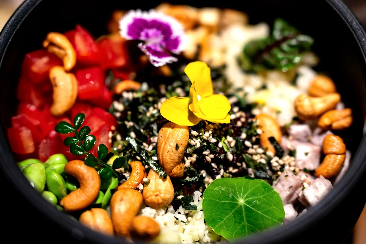 A rice bowl topped with vegetables, seeds and edible flowers
