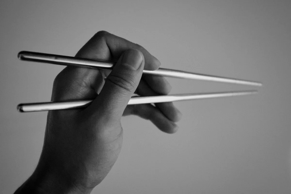 A hand holding a pair of chopsticks in the conventional grip