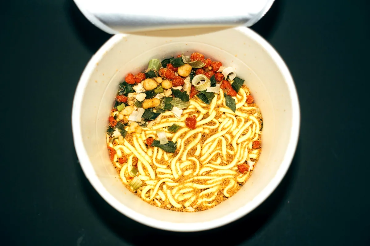 A bowl of instant noodles dressed with vegetables and herbs
