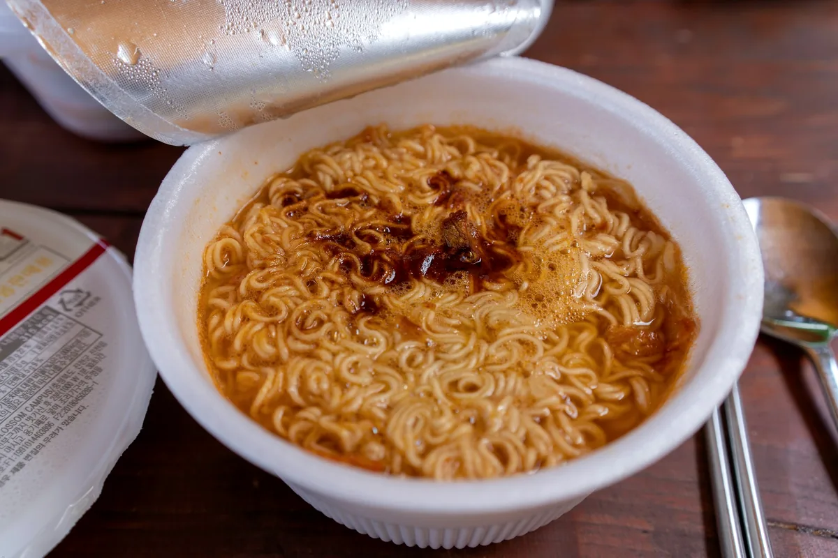 Prepared instant noodles in a bowl beside the packet they came from