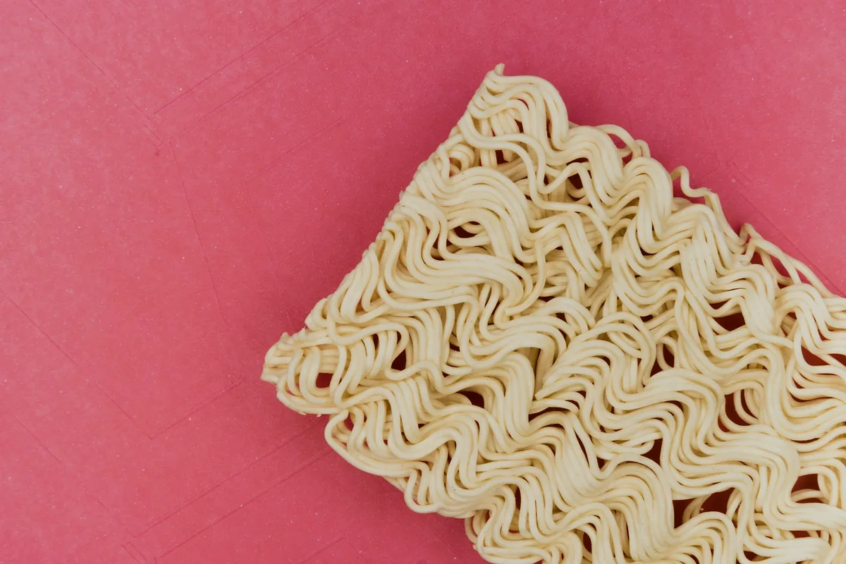 A rectangular block of dried instant noodles on a pink background