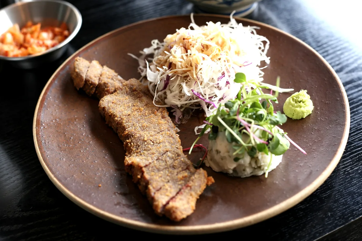A sliced breaded cutlet plated with finely shredded cabbage and potato salad