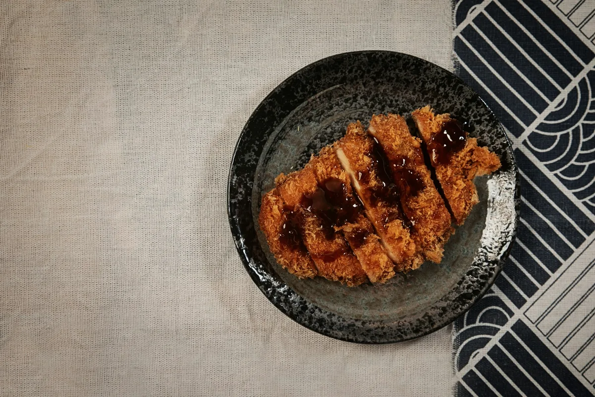 Strips of breaded cutlet arranged in a dark bowl with sauce brushed over the top