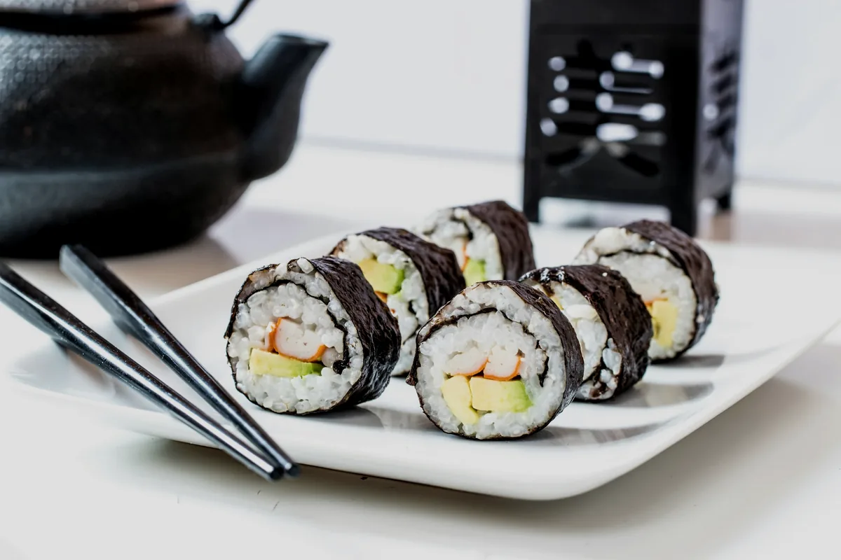 Cut vegetable rolls on a white plate beside a cast-iron teapot
