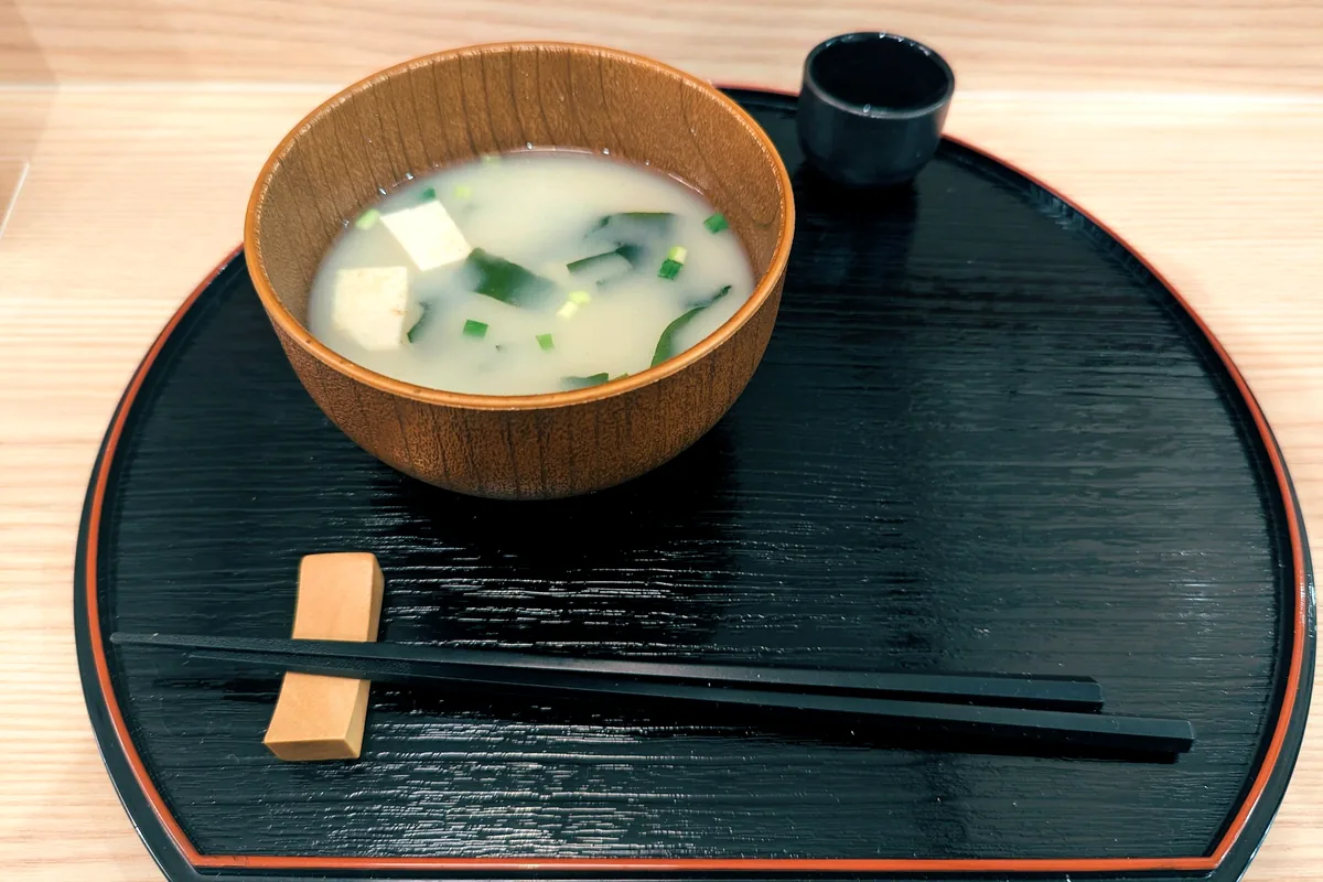 A wooden bowl of miso soup set on a black tray with chopsticks
