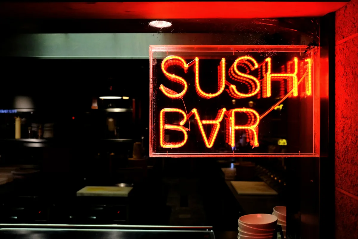 A neon sign reading Sushi Bar above a dark restaurant frontage