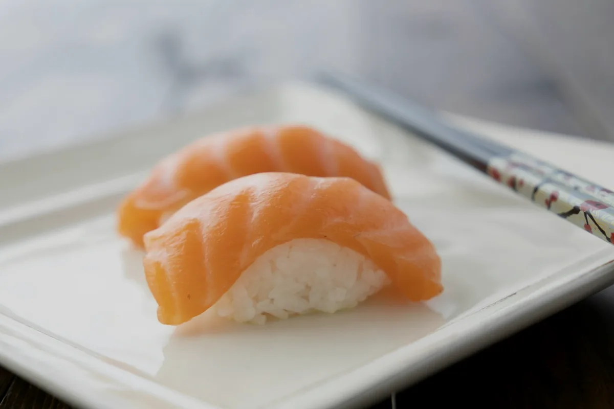 Two pieces of salmon nigiri on a white plate with chopsticks