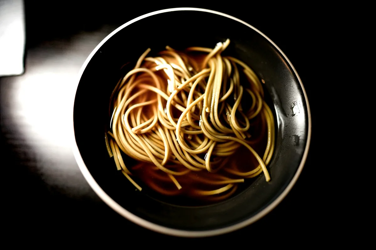 A dark bowl of thin noodles photographed from above
