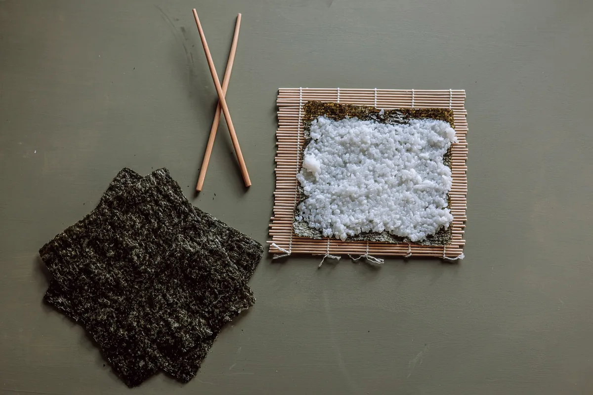 A sheet of nori laid on a bamboo rolling mat beside chopsticks