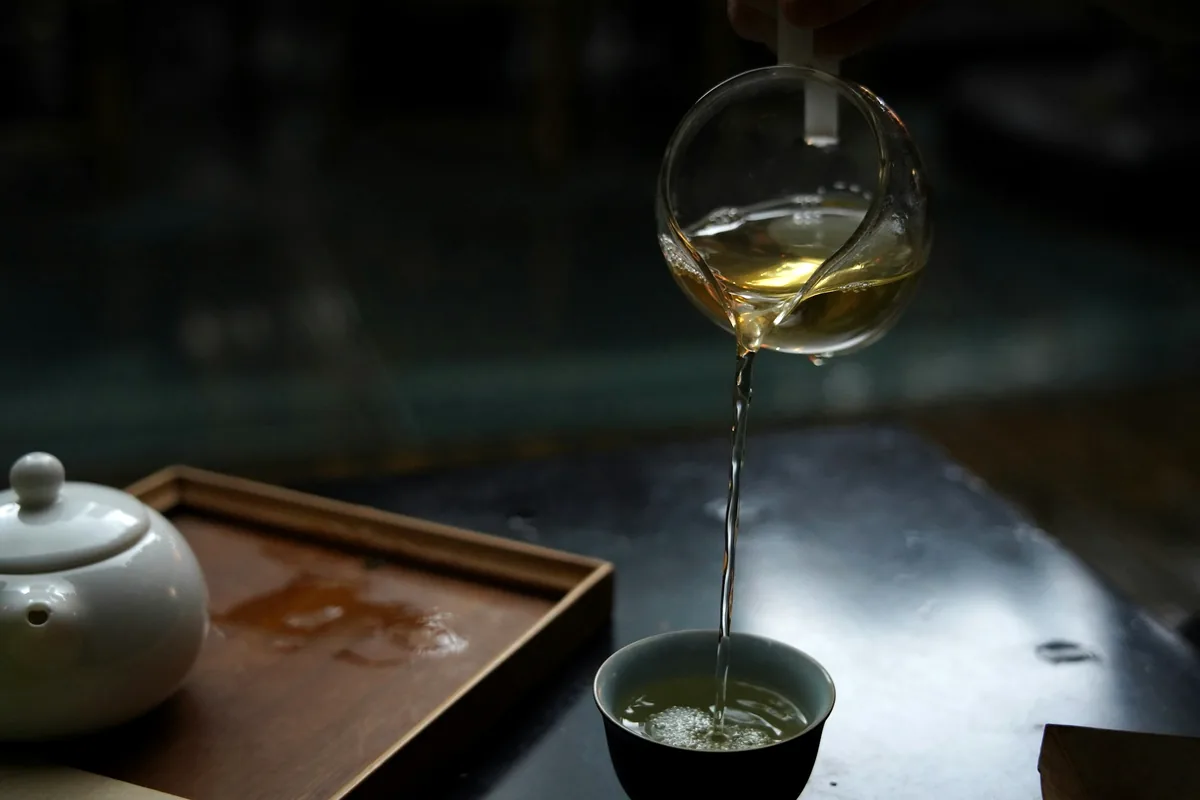Green tea being poured into a small cup on a dark table