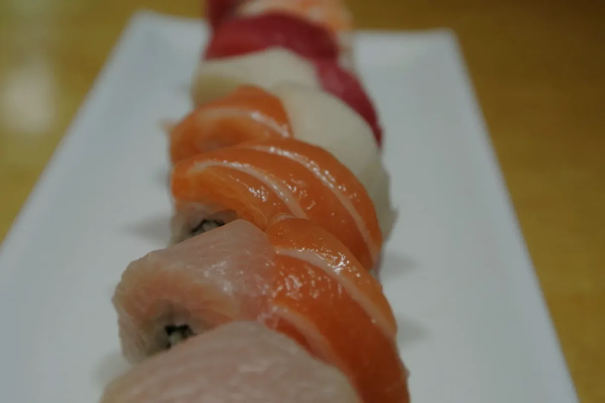 Rainbow Roll topped with overlapping slices of fish on a white plate