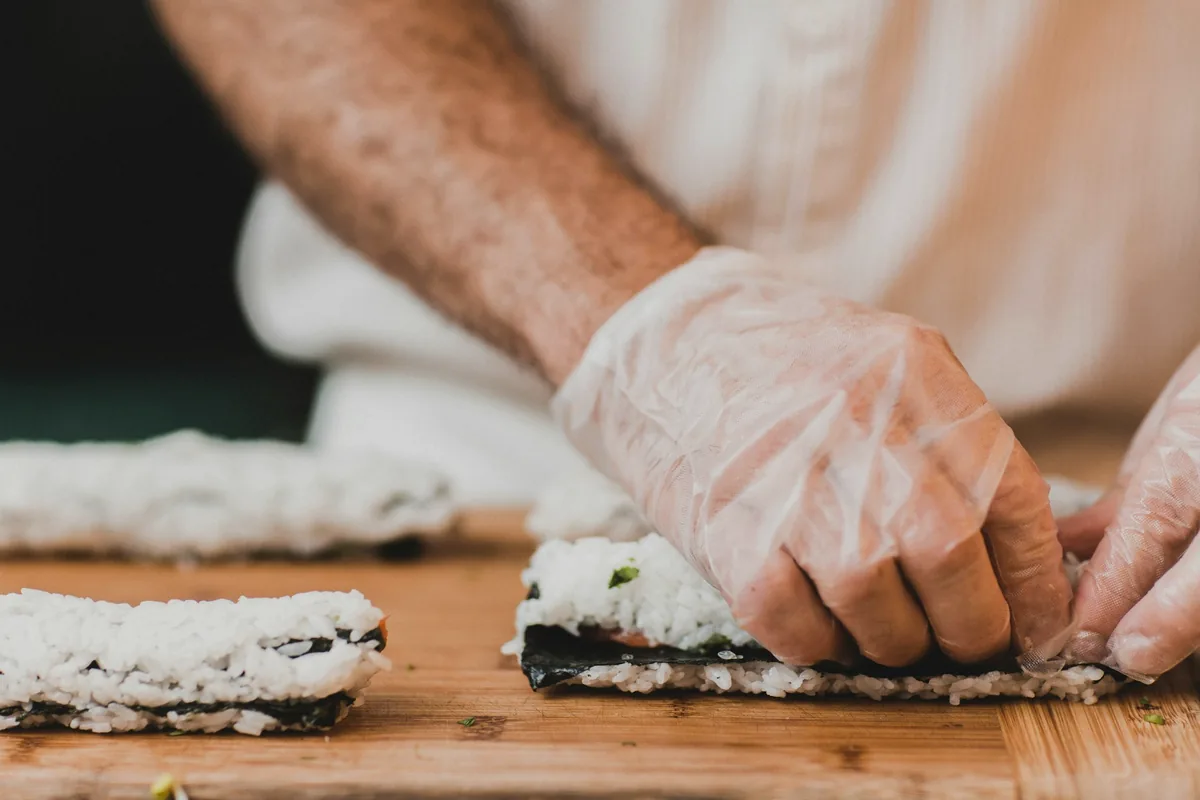 Hands spreading rice over nori on a bamboo rolling mat