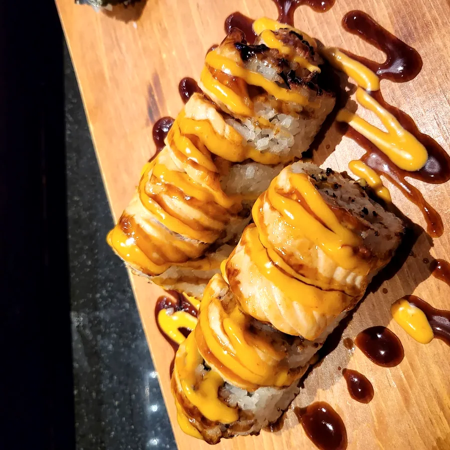 Baked Alaskan roll with baked salmon and sauce on a wooden board