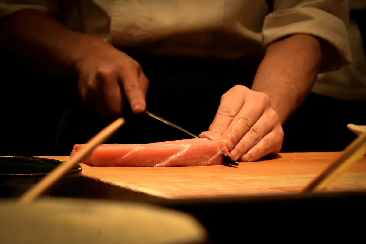 Hands drawing a knife through a block of salmon on a wooden board