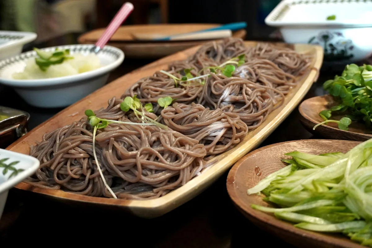 Grey-brown buckwheat noodles served on a wooden tray with green onion
