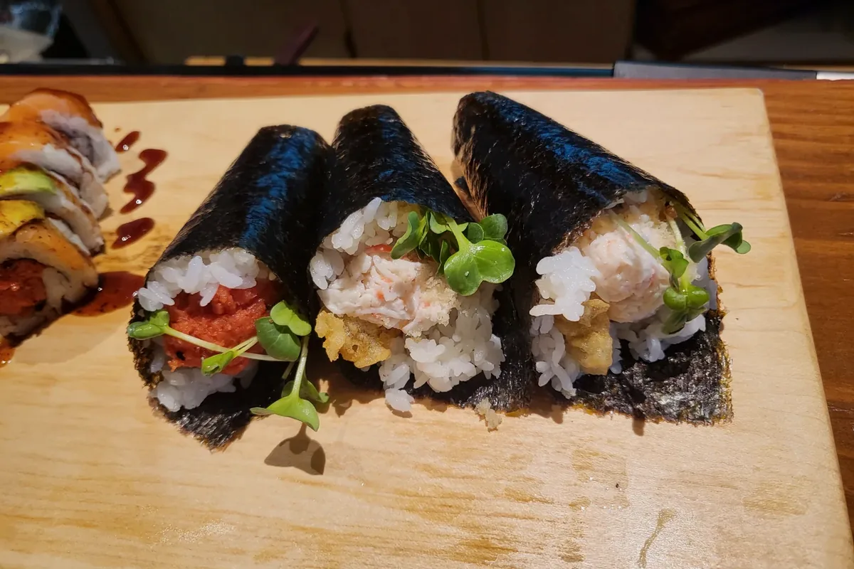 Spicy scallop hand rolls wrapped in nori cones on a wooden board