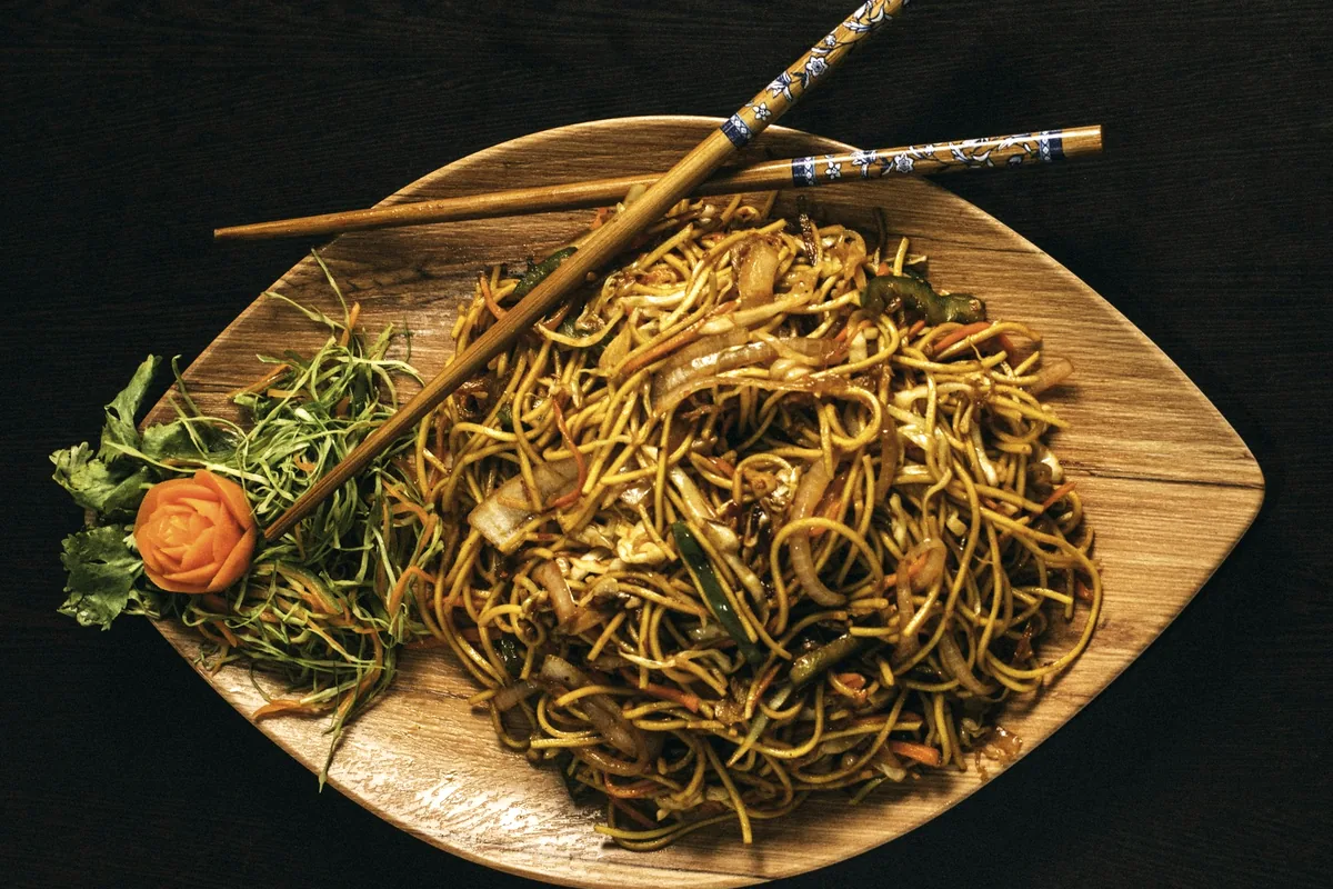 Stir-fried noodles served on a wooden dish with chopsticks resting across it