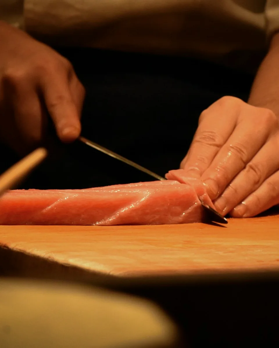 A chef slicing a loin of tuna on a wooden board under warm light